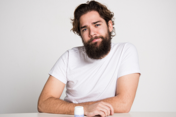 A man staring at the camera. In front of him on the table is a bottle of prep-pills.